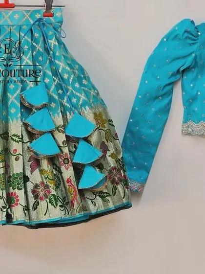 A designer lehenga with a long-sleeved turquoise blouse and a matching skirt with a floral border. The blouse features delicate embroidery.