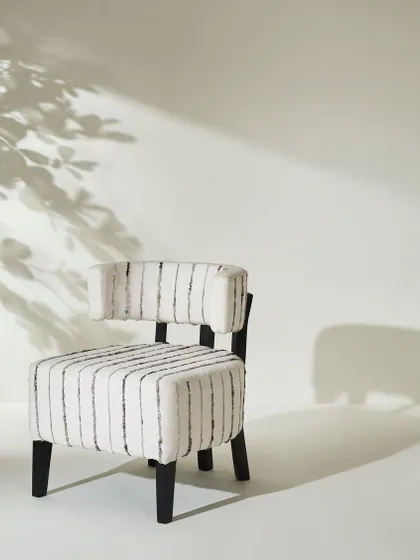 A uniquely shaped accent chair with striped upholstery, isolated against a white background with artistic shadows. This is a high-impact, minimalist shot perfect for a catalog cover or feature page.
