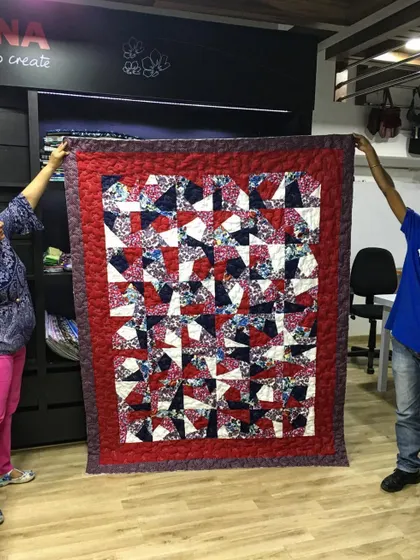 Our clients holding up a finished scrappy quilt with a modern, abstract design.