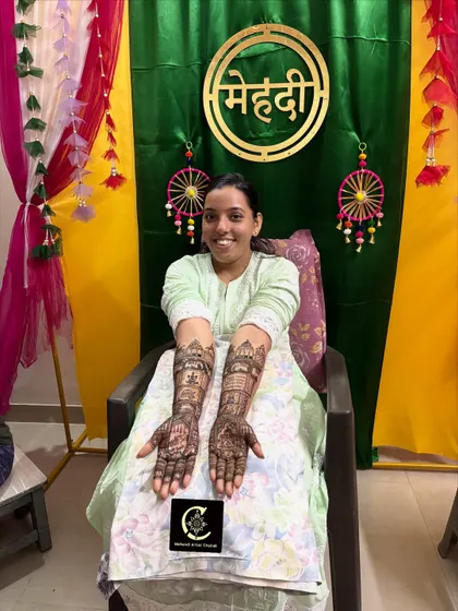 A happy bride showing her full-arm bridal mehendi. This design features detailed story-telling elements, including figures and traditional motifs, created with my homemade organic henna cones for a rich, dark stain.