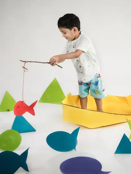 A different angle of the imaginative fishing trip. The little boy proudly shows off the paper fish he "caught" from his paper boat.