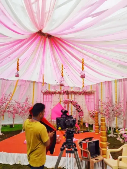 A view from behind the camera of a pink-themed mandap being set up, showing the extensive fabric draping and floral details.