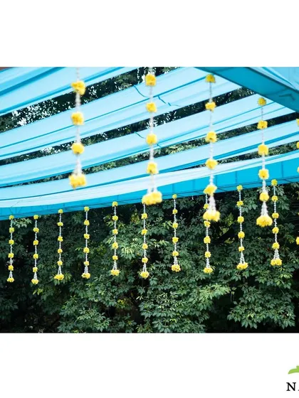 A detail shot of the hanging floral strings used in the Haldi decor. The combination of yellow marigolds and white jasmine against the blue canopy added a delicate and festive touch to the outdoor setting.
