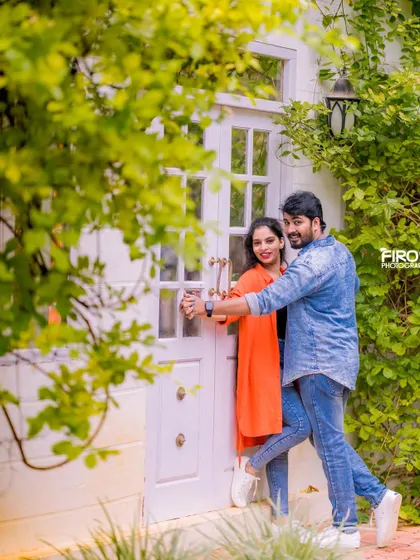 A fun, dancing pose in front of a white door, framed by green leaves. The couple's casual outfits and their joyful interaction make this a great shot.