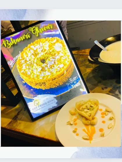 A taste of Rajasthan with our Bikaneri Ghevar. This disc-shaped sweet is soaked in sugar syrup and topped with rabri and nuts, offering a crispy and sweet bite.