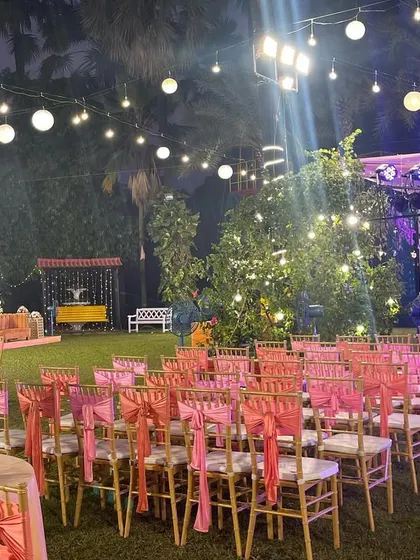 A view of the guest seating area for a reception, with the stage in the background. The pink chair sashes and warm lighting create a welcoming and festive atmosphere.