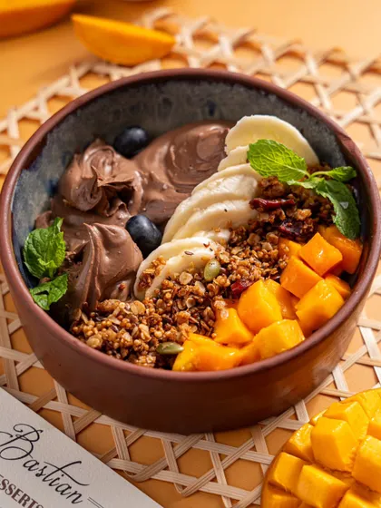 A healthy yet delicious mango smoothie bowl from Bastian. This image appeals to health-conscious diners, showcasing fresh fruit, granola, and chocolate.