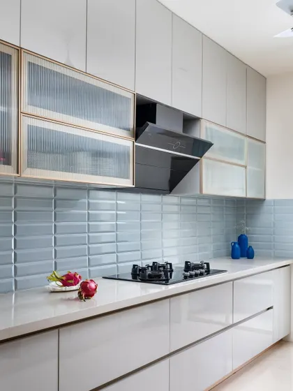 The kitchen features a serene pastel blue tile backsplash, handleless cabinetry for a clean look, and fluted glass overhead storage that adds texture while keeping the space feeling light.