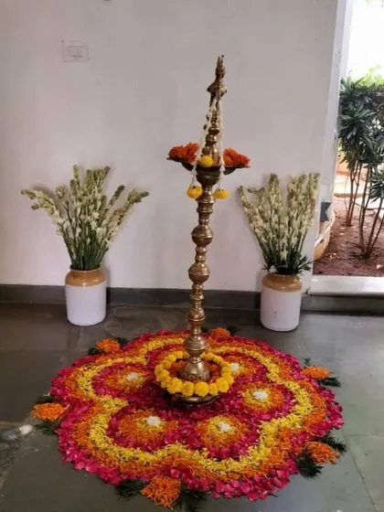 A traditional brass lamp (diya) placed in the center of a colorful floral rangoli, creating a beautiful and symbolic focal point for a ceremony.