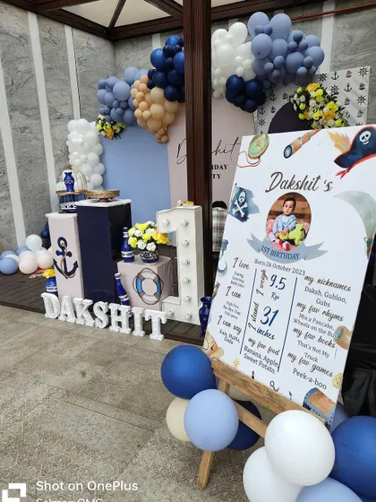 A full view of the boat-themed decor, including the personalized backdrop and a chalkboard-style milestone board detailing the birthday boy's first year.