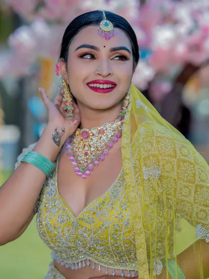 A joyful bride in a bright yellow lehenga. The makeup is fresh and vibrant, with pink and gold tones that match her stunning Kundan jewelry.