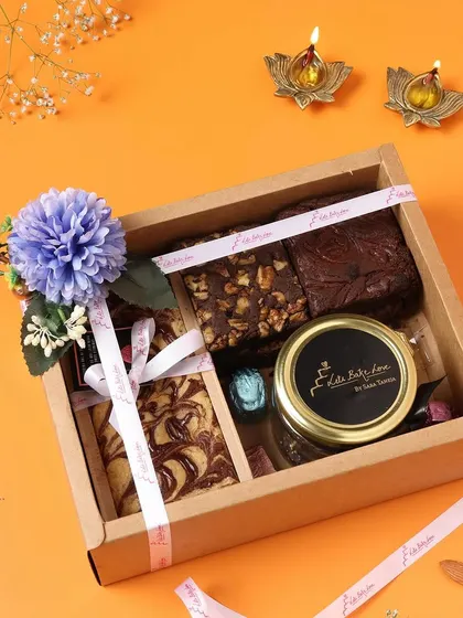 A rustic yet elegant cardboard gift box filled with a tea cake, brownies, and a jar of goodies for Diwali.
