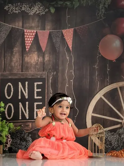 A rustic and charming first birthday setup. The wooden backdrop, chalkboard sign, and colorful flowers create a warm and celebratory atmosphere.