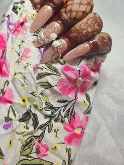 The details make the design. This close-up shows how the delicate 3D flowers and chain accessories on the nails are designed to match the floral patterns in the bride's attire.