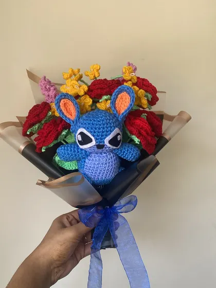 For the fans of 'Ohana'! I had so much fun making this custom Stitch bouquet. The little blue character is nestled among vibrant red and yellow crochet flowers, all wrapped in stylish black and gold paper. It’s a perfect example of how we can bring your favorite characters to life.