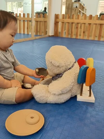 A toddler shares his toys with a teddy bear, an early form of role-play that shows developing social and emotional skills.