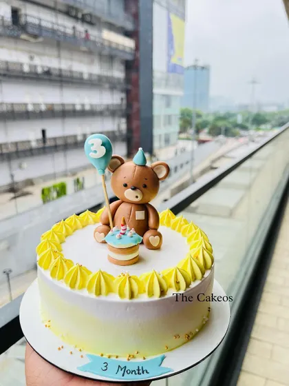 A charming mini cake designed to celebrate a three-month milestone. This cake features a handcrafted fondant teddy bear holding a balloon, sitting atop a delicately frosted cake.