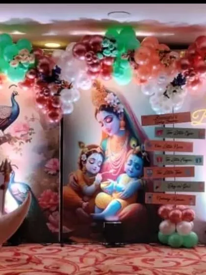 A beautiful baby shower stage with a Krishna theme. The decor includes a large moon prop, character cutouts, and a balloon arch in pastel colors.
