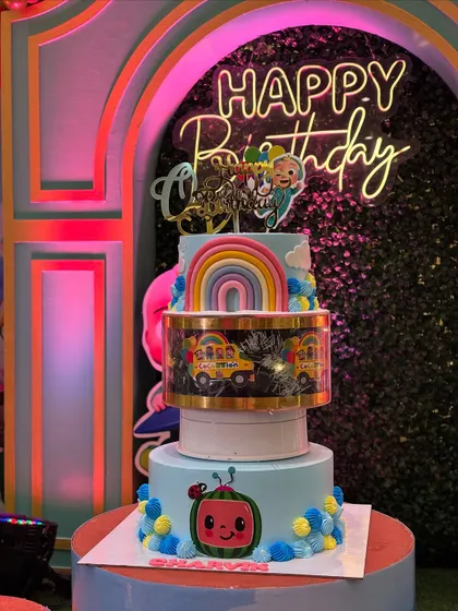 A stunning Cocomelon cake set against a party backdrop with a neon "Happy Birthday" sign. This shows how my cakes can be the highlight of any party setup.