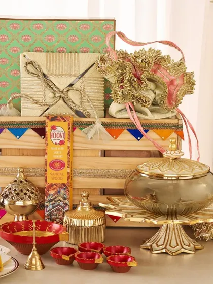 I designed this festive hamper with a mix of traditional and decorative items, including a brass incense holder, a lidded serving dish, colorful diyas, and beautifully wrapped gifts in a decorated wooden crate.
