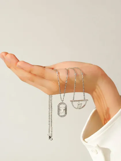 A hand delicately holds a collection of silver necklaces, showcasing their different designs and lengths. The clean, minimalist styling puts the focus entirely on the intricate details of the jewellery.