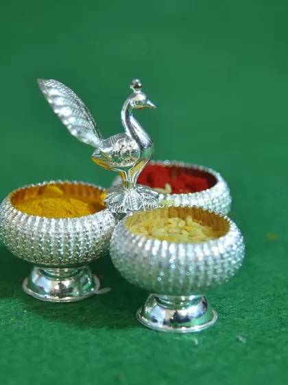 A duplicate of image 18, this shot focuses on the silver peacock arishina kumkuma set against a solid green background, highlighting its intricate design.