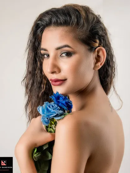 A bare-shouldered beauty shot where the model holds a bouquet of blue roses. Her direct gaze and the vibrant color of the flowers create a striking and serene portrait.