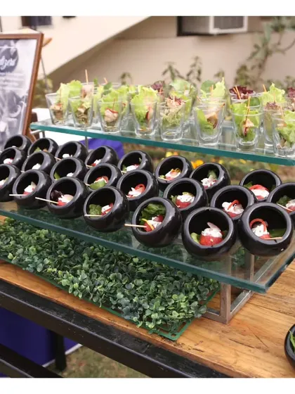 A display of assorted cold canapés, including fresh salads in shot glasses and cheese bites in black ceramic bowls.