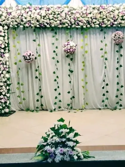 A simple yet elegant stage setup with a floral arch and hanging ivy against a white curtain. The blue fabric accents add a pop of color to this clean and fresh design.
