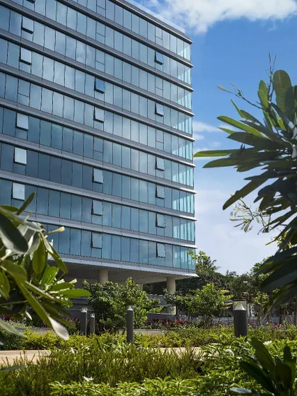 The glass facade of the Godrej Centre Development, featuring operable windows that give users control over their immediate environment. The building is framed by mature trees, demonstrating our commitment to biophilic modern workspace ideas.