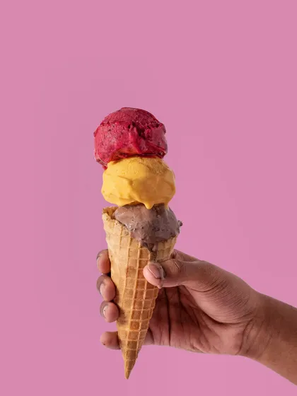 A triple-scoop ice cream cone held against a solid pink background. This is a classic, eye-catching product shot that is both simple and highly effective for any ice cream brand.