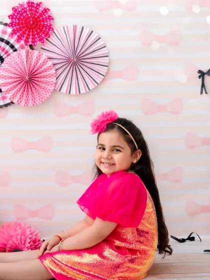 A sweet, seated portrait of a girl in a pink sequin dress, her happy smile lighting up the room.