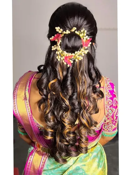 A beautiful half-up hairstyle with defined curls on highlighted hair. The look is completed with a delicate floral and pearl hair accessory, adding a touch of elegance.