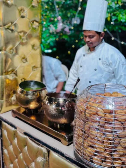 A chef at the chaat station preparing pani puri, with a large container of crispy puris ready to be filled.