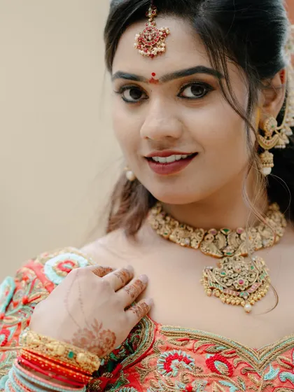 A close-up portrait of a smiling bride, highlighting her beautiful makeup and traditional gold jewelry.