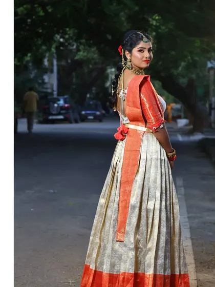 A beautiful tissue silk half saree in cream and orange, paired with a handcrafted blouse. This outfit is perfect for outdoor photoshoots and daytime events.
