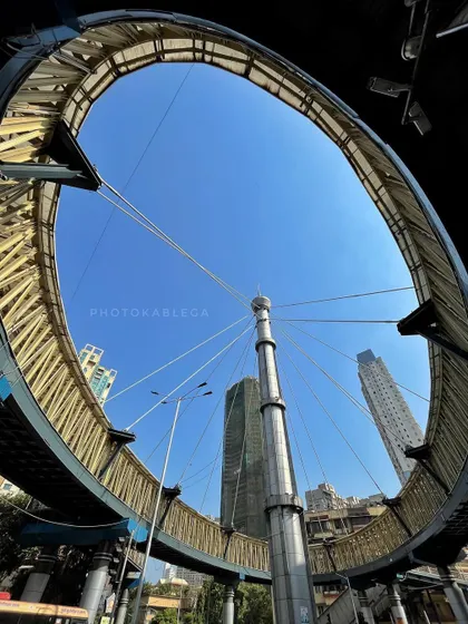 A creative, worm's-eye view of the circular skywalk at a busy Mumbai intersection, showcasing its unique design against the blue sky.