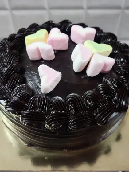 A dark chocolate cake decorated with a piped border and topped with heart-shaped marshmallows.