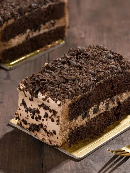 A slice of rich chocolate pastry, styled with dramatic side lighting to highlight its layers. This moody shot creates a sense of indulgence and premium quality.