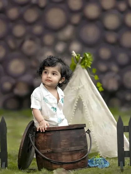 A little explorer in our rustic camping setup, peeking out from behind a wooden barrel. We love capturing their playful curiosity.