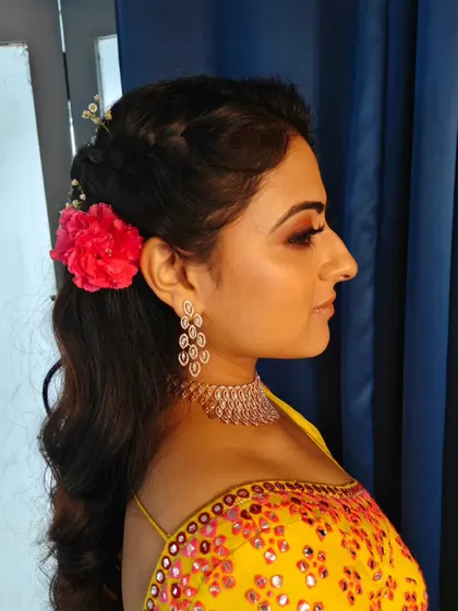 A side profile of the Haldi hairstyle. The combination of the braid, soft waves, and fresh flower is simply beautiful.