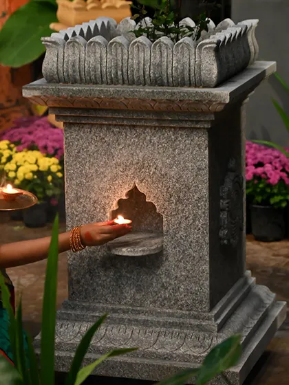 A diya is placed in the niche of a granite Tulasi Brindavan, symbolizing the light and blessings it brings to a home.