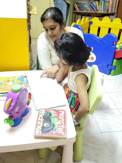 A mother helps her daughter explore a new book at one of our kid-sized tables. We've created a comfortable environment for families to learn and grow together.