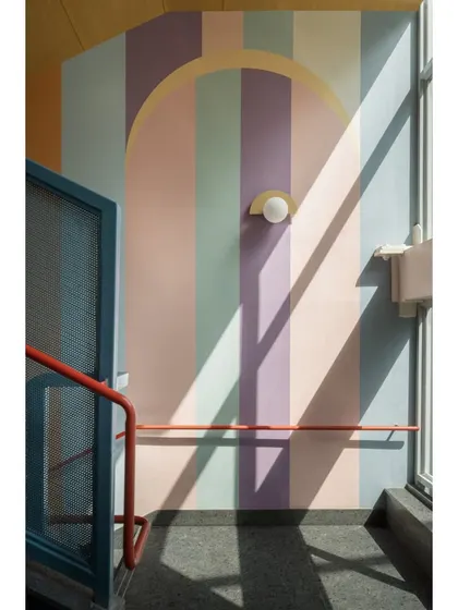 Sunlight creates beautiful shadows across a pastel-striped wall in a stairwell. We used color and light to turn these transitional spaces into moments of unexpected beauty.