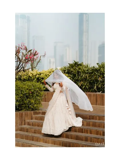 A playful and ethereal shot of the bride with her veil flowing in the wind against a city skyline. It's a modern, dynamic, and beautiful bridal portrait.