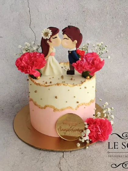This anniversary cake is all about romance and detail. It features a hand-sculpted kissing couple topper, a soft pink and white color palette, and is decorated with fresh carnations and baby's breath.