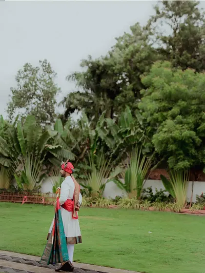 A portrait of the groom in his traditional Maharashtrian wedding attire, complete with a colorful pheta and shawl, standing proudly before the ceremony.
