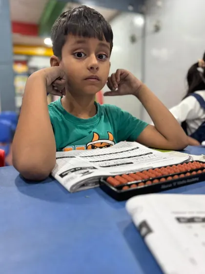 A young student looks up from his worksheet, deep in thought. Abacus training is all about building these moments of deep concentration.