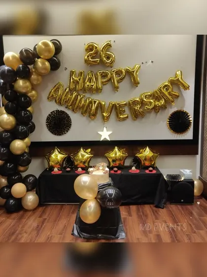 A classic and elegant 26th-anniversary decoration. This setup features a black and gold theme with a balloon garland and large 'Happy Anniversary' foil letters.