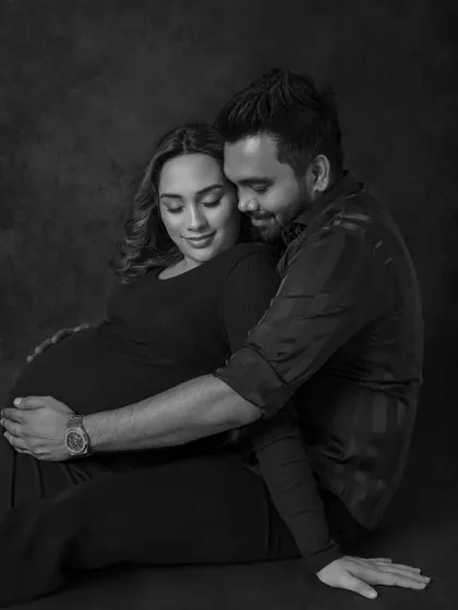 A cozy and intimate portrait. The couple is seated on the floor, wrapped in a loving embrace, creating a feeling of warmth, safety, and quiet anticipation for their new arrival.